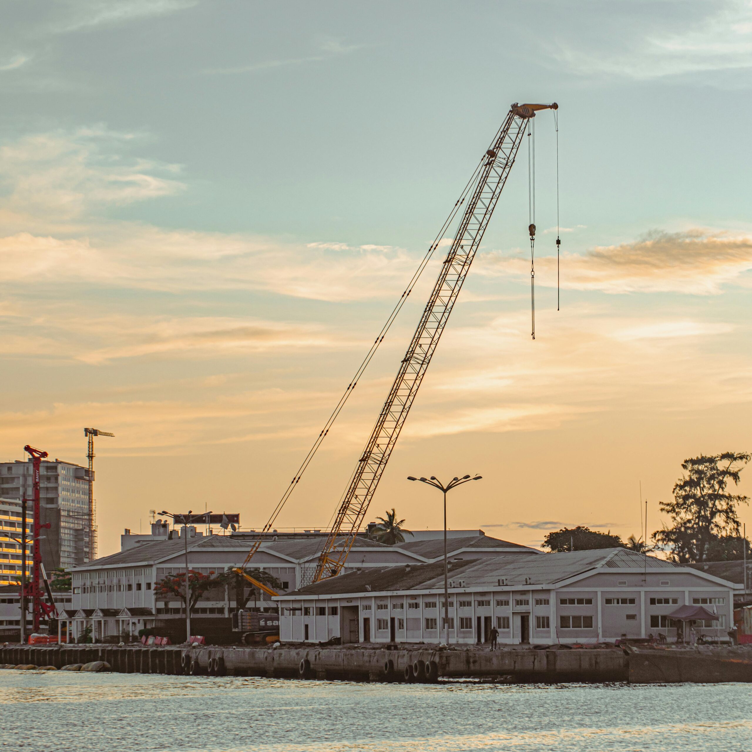A scenic view of Luanda Harbor at sunset featuring a prominent crane and industrial buildings.