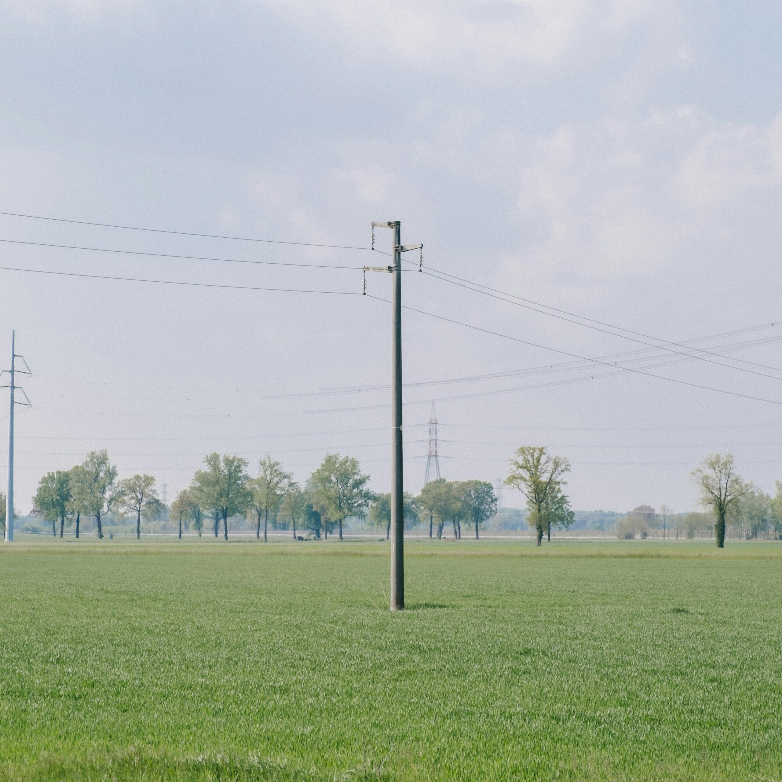 Scenic view of power lines over a vast green field with cloudy sky.